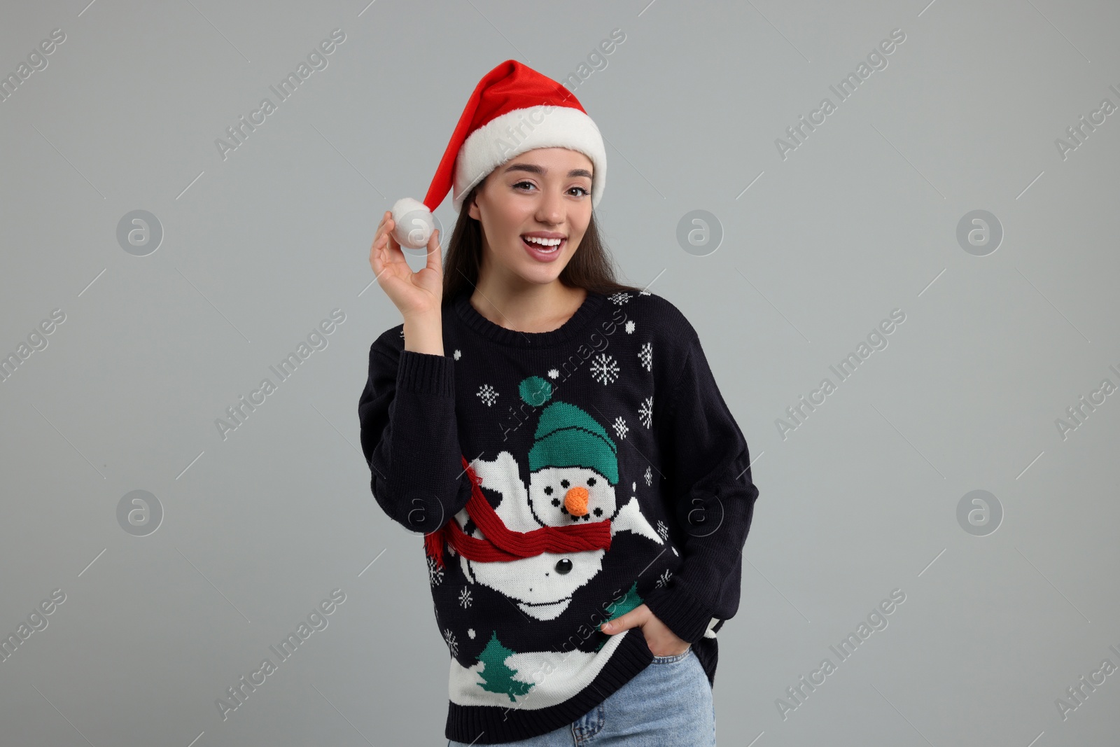 Photo of Happy young woman in Christmas sweater and Santa hat on grey background