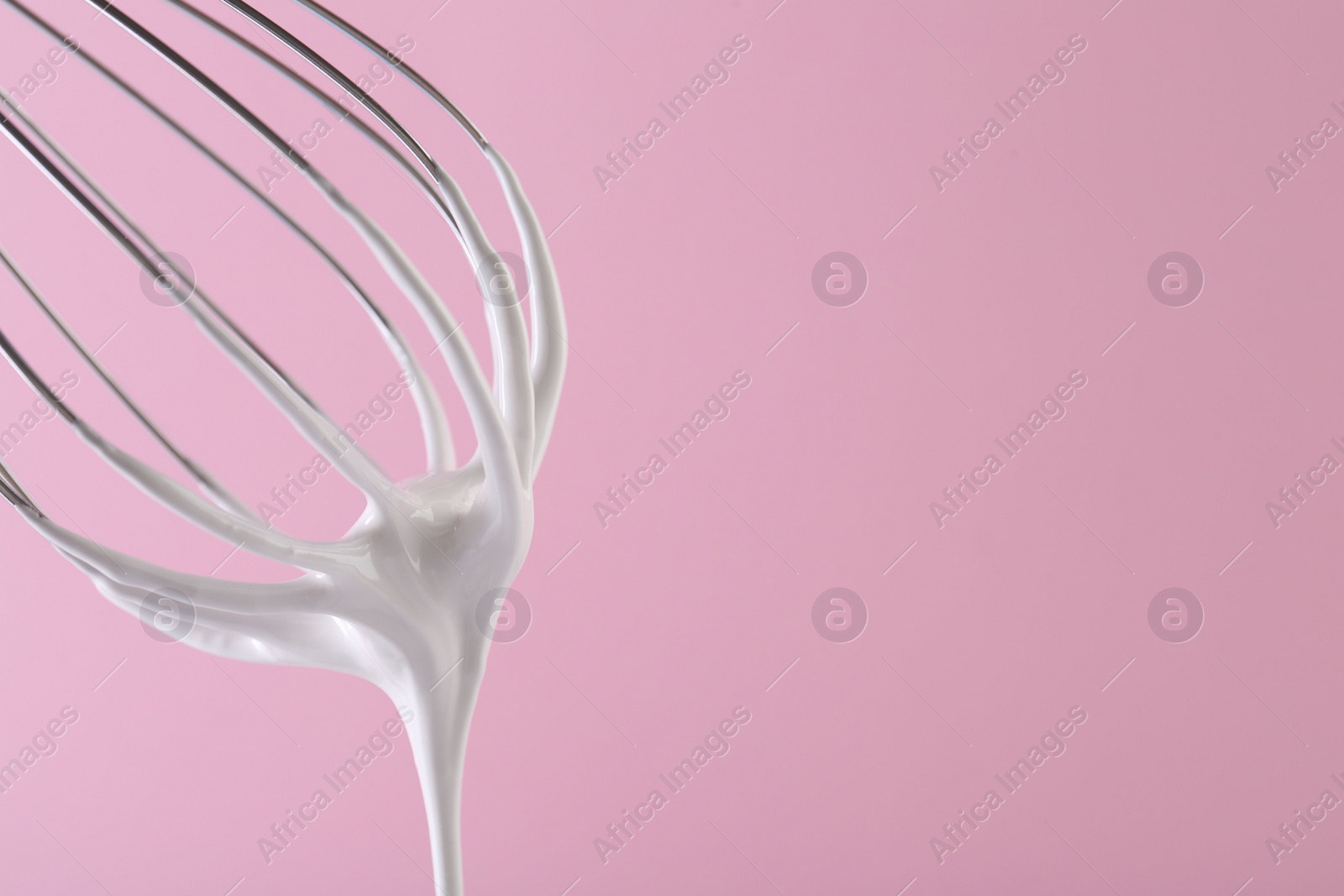 Photo of Whisk with whipped cream on pink background, closeup. Space for text