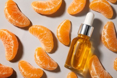 Aromatic tangerine essential oil in bottle and citrus fruit on grey table, flat lay