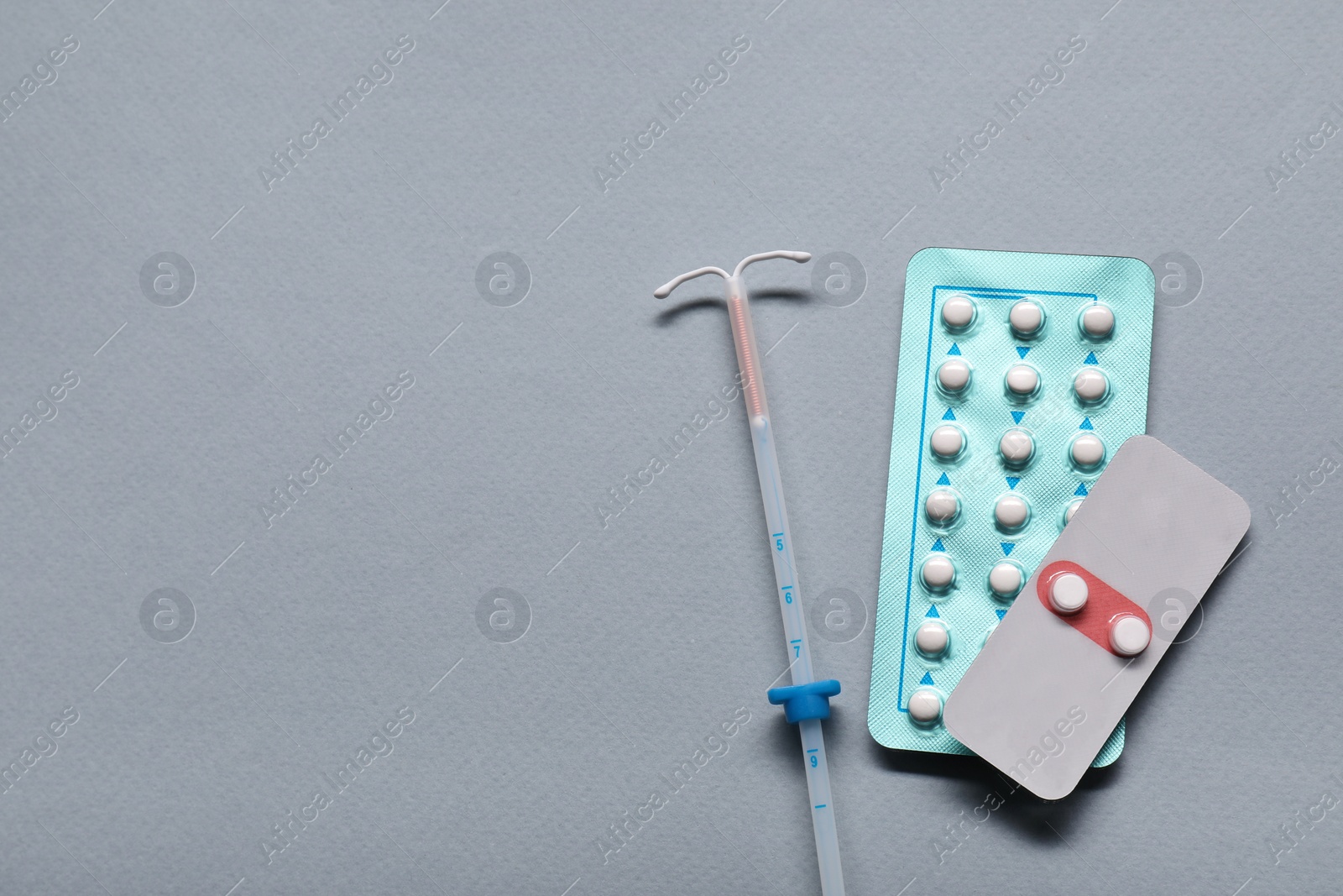 Photo of Birth control pills and intrauterine device on light grey background, flat lay and space for text. Choosing method of contraception