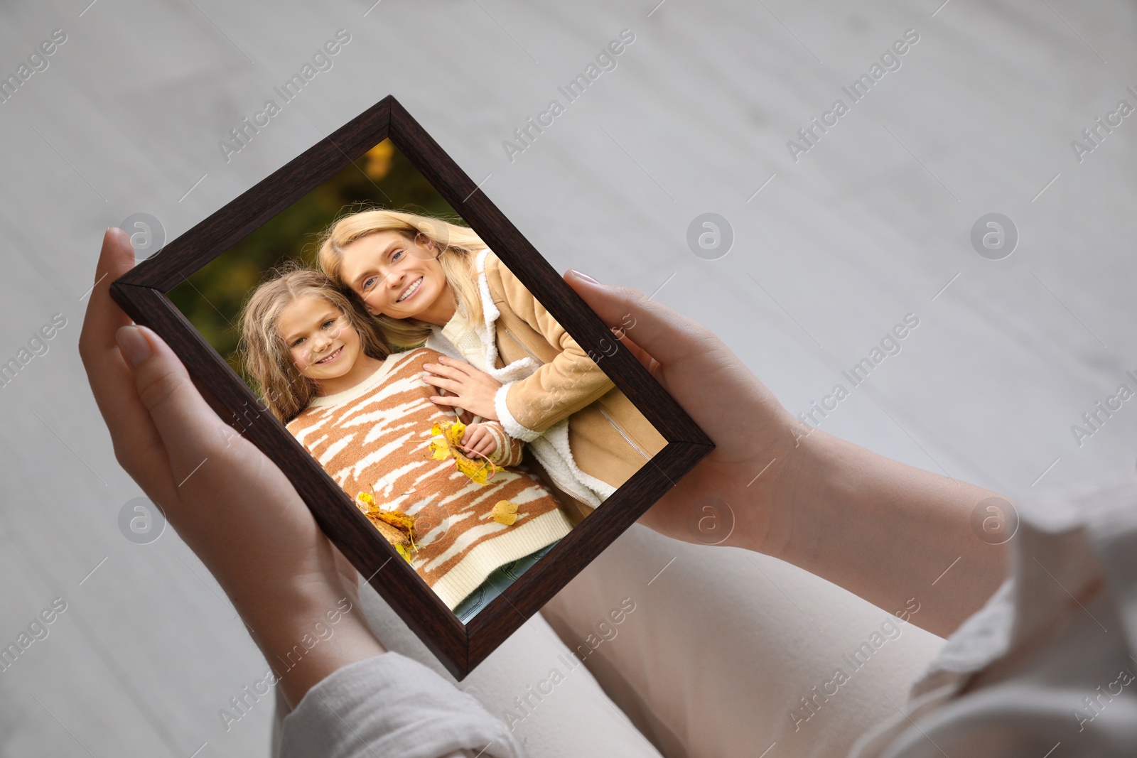 Image of Woman holding frame with photo portrait of her family indoors, closeup