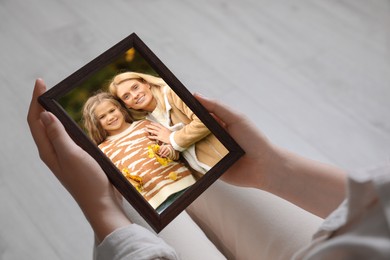 Woman holding frame with photo portrait of her family indoors, closeup