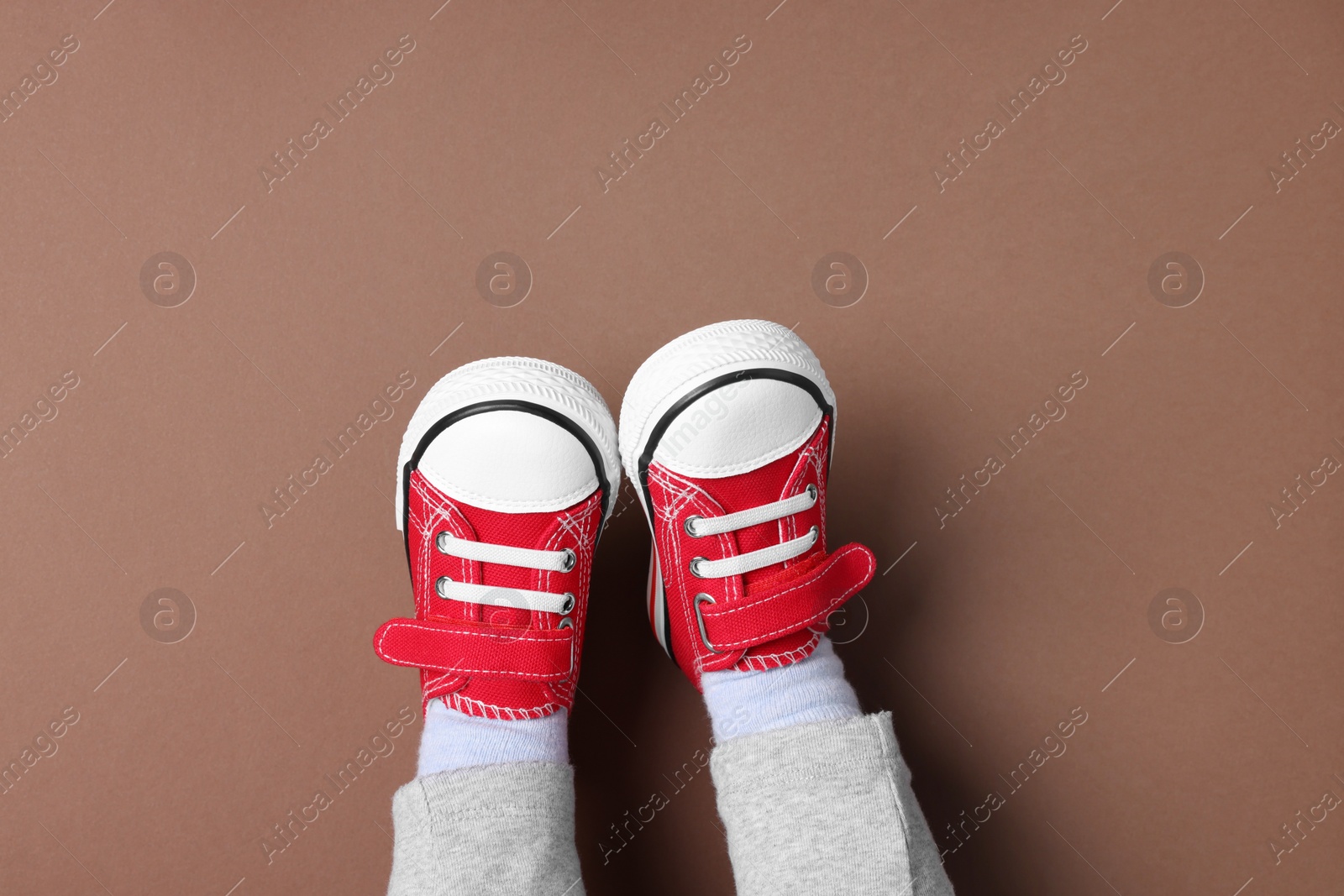 Photo of Little child in stylish red gumshoes on brown background, top view