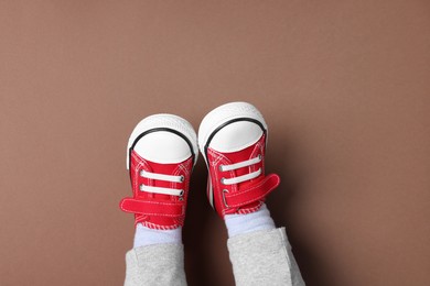 Photo of Little child in stylish red gumshoes on brown background, top view