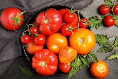 Photo of Many different ripe tomatoes with leaves on black table, flat lay