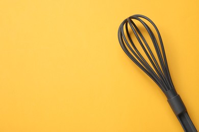 Plastic whisk on yellow background, top view. Space for text