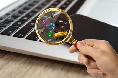 Woman with magnifying glass detecting microbes on laptop keyboard, closeup