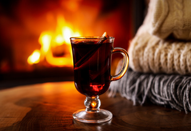 Photo of Tasty mulled wine, knitwear and blurred fireplace on background