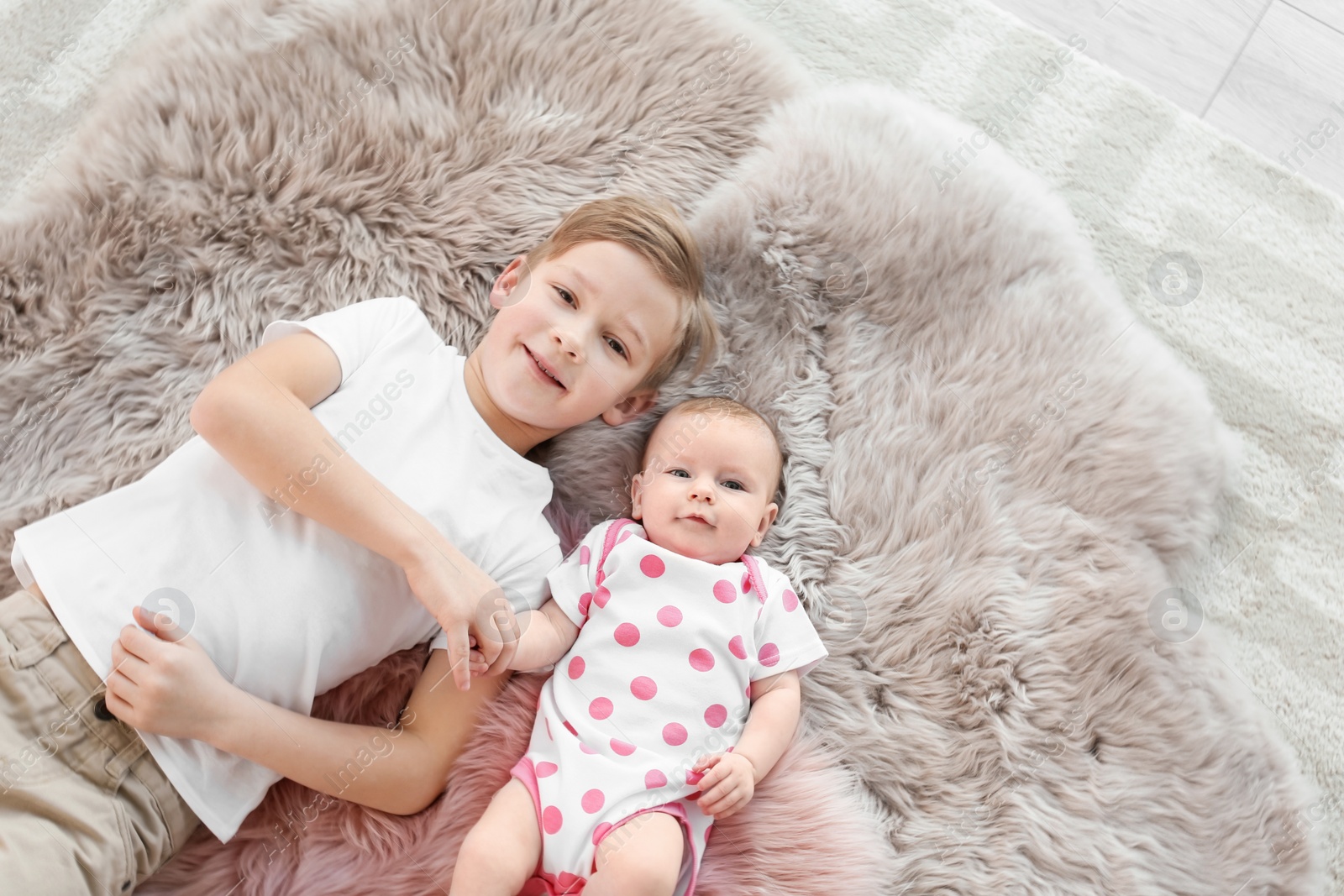 Photo of Cute little baby with elder brother lying on soft fluffy plaid at home