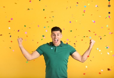 Emotional man and falling confetti on yellow background