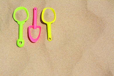 Colorful plastic shovels on sand, space for text. Beach toys