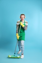 Photo of Handsome young man with headphones and mop singing on light blue background