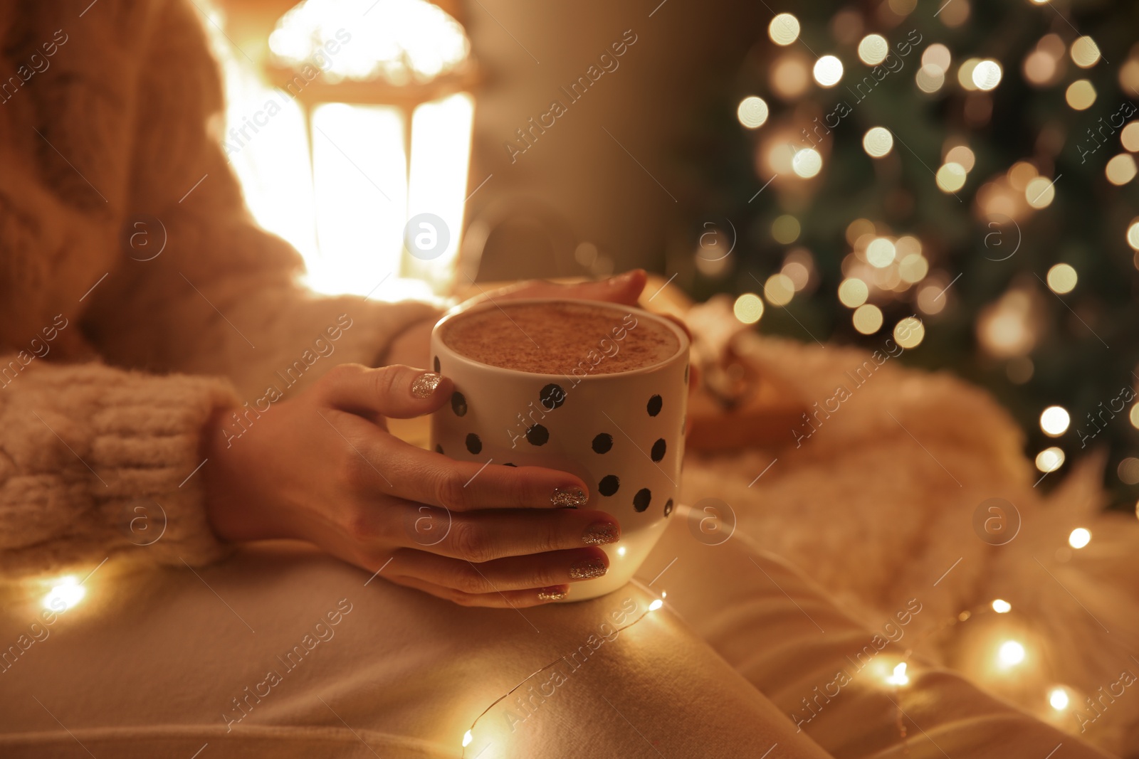 Photo of Woman with cup of hot drink near Christmas tree at home, closeup
