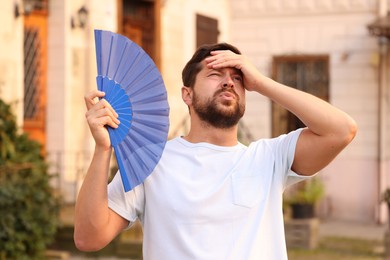 Man with hand fan suffering from heat outdoors