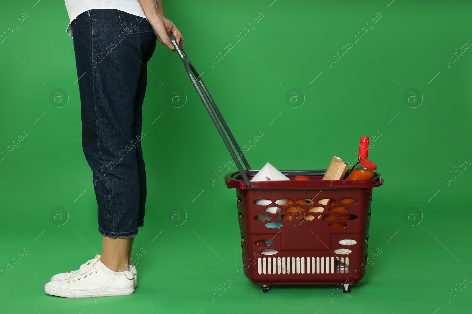 Photo of Woman with shopping basket full of different products on green background, closeup