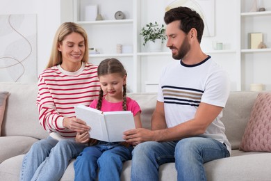 Photo of Happy family reading book together on sofa at home