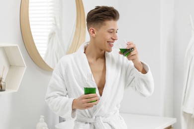 Photo of Young man using mouthwash in bathroom. Oral hygiene