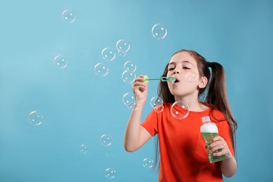 Little girl blowing soap bubbles on light blue background, space for text