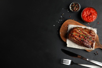 Photo of Grilled meat served with garnish and sauce on black table, flat lay. Space for text