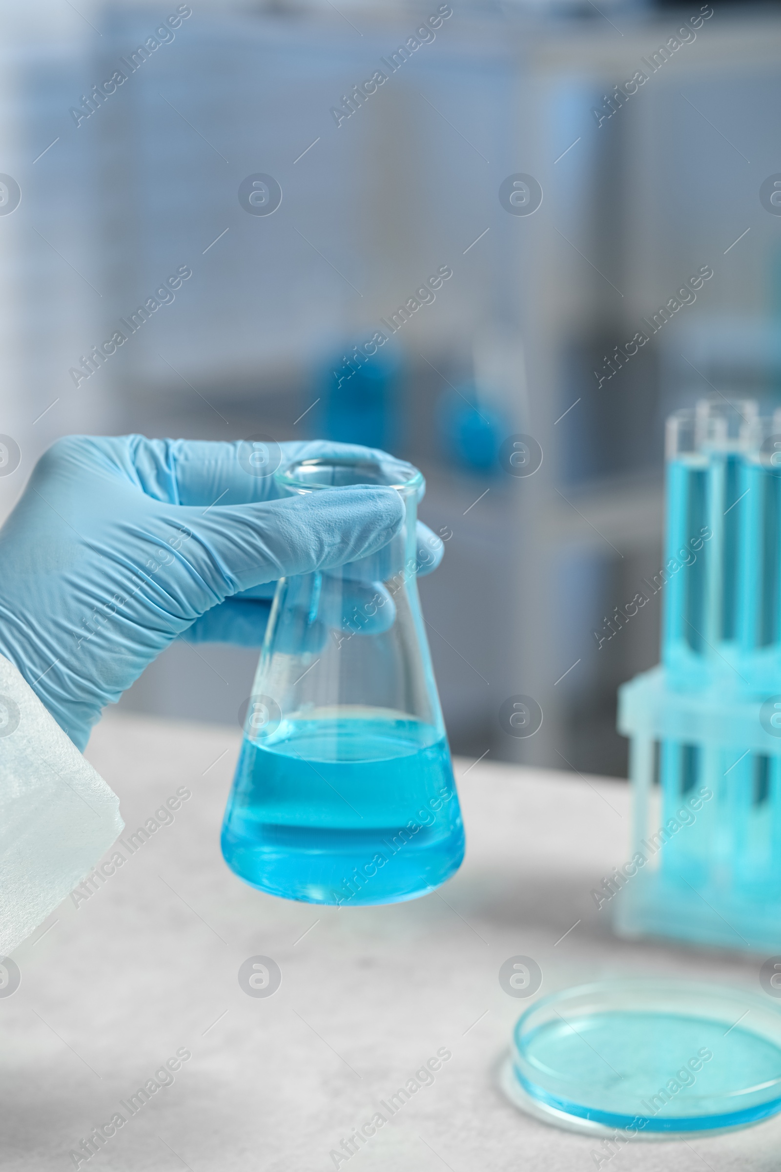 Photo of Scientist with beaker of light blue liquid in laboratory, closeup