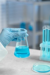 Photo of Scientist with beaker of light blue liquid in laboratory, closeup