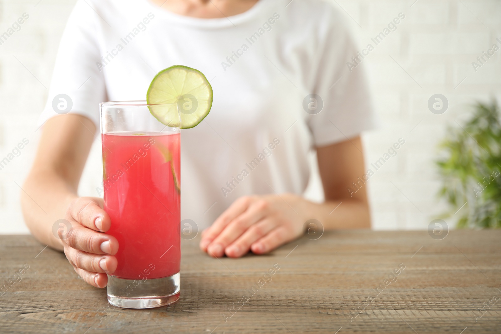 Photo of Young woman with glass of tasty refreshing drink at wooden table, closeup