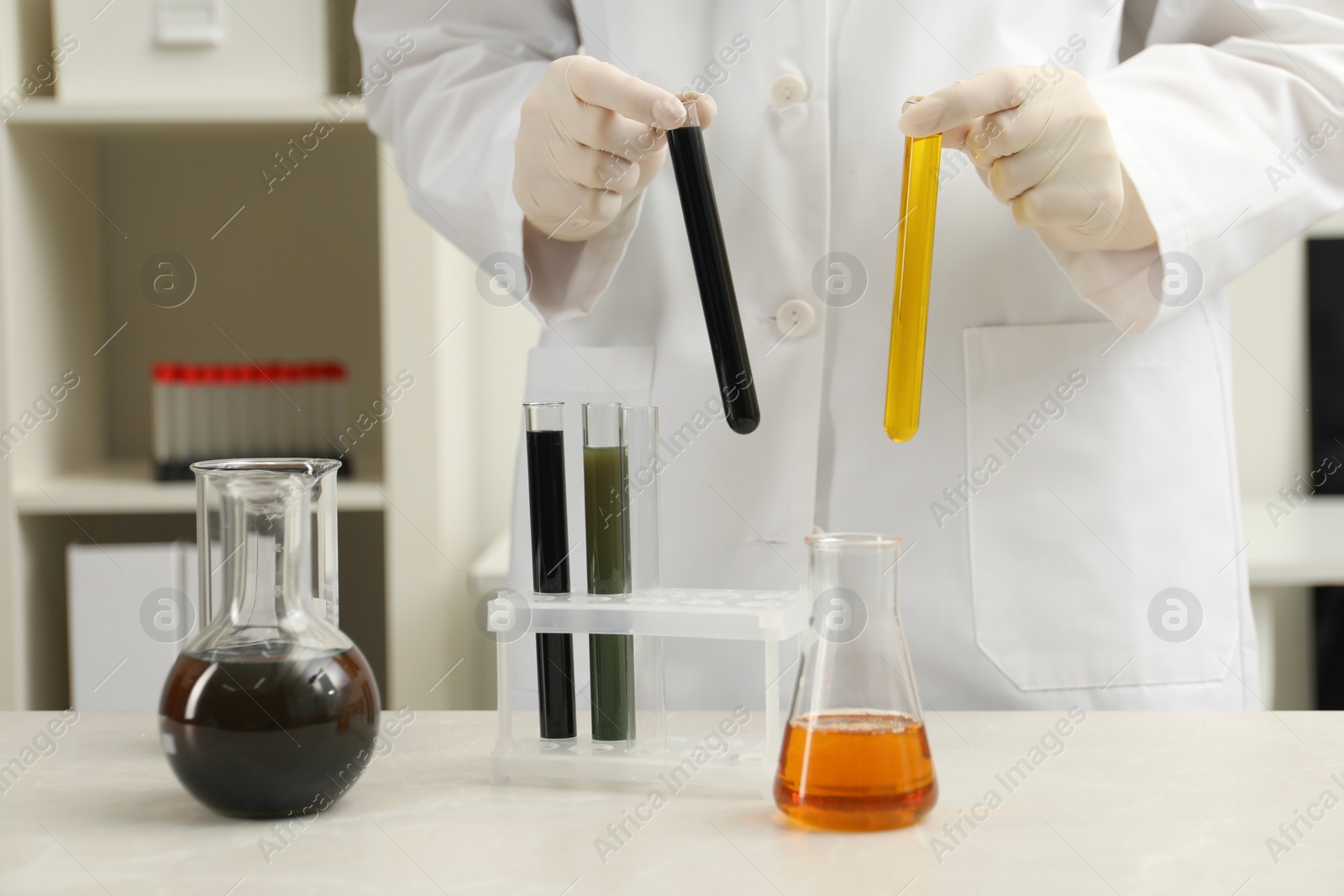 Photo of Laboratory worker holding test tubes with different types of crude oil at light marble table, closeup