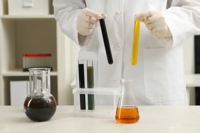 Laboratory worker holding test tubes with different types of crude oil at light marble table, closeup