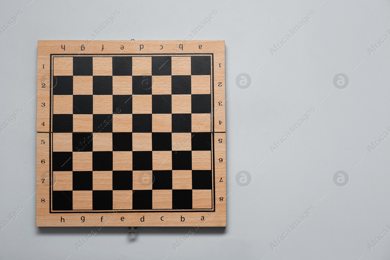 Photo of Empty wooden checkerboard on light grey background, top view. Space for text