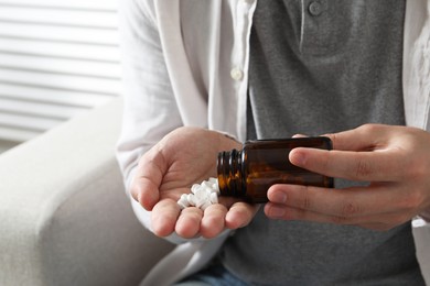 Man pouring pills from bottle on blurred background, closeup