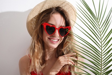 Photo of Young beautiful woman wearing heart shaped glasses and tropical palm leaf on white background