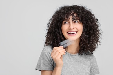 Photo of Young woman holding teeth whitening strips on light grey background, space for text