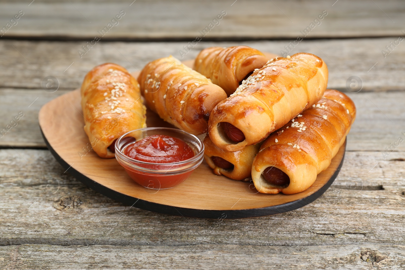 Photo of Delicious sausage rolls and ketchup on wooden table