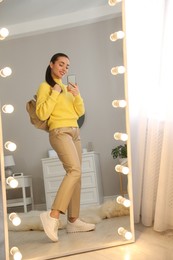 Young woman taking mirror selfie in stylish outfit at home. Morning routine