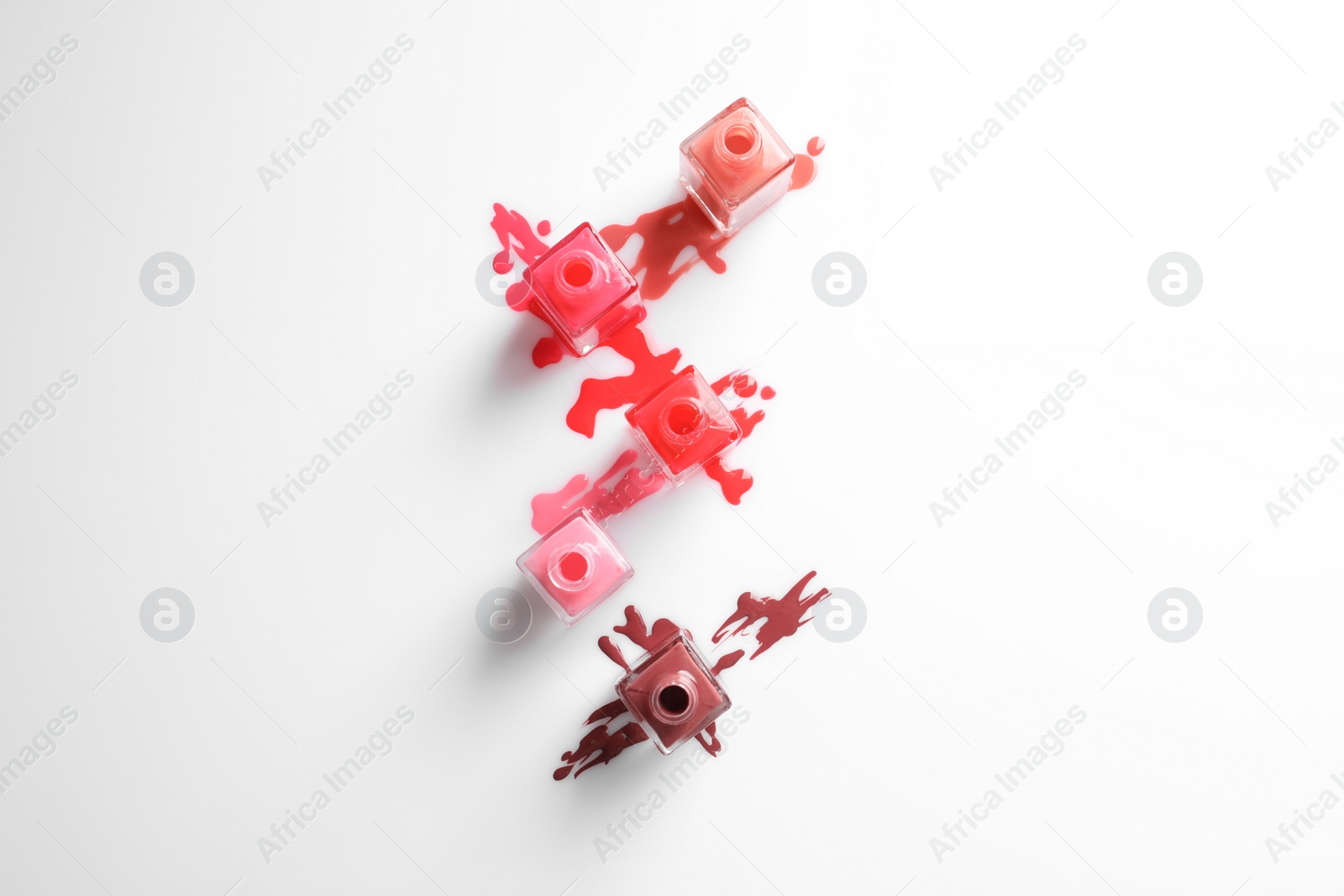 Photo of Spilled different nail polishes with bottles on white background, top view