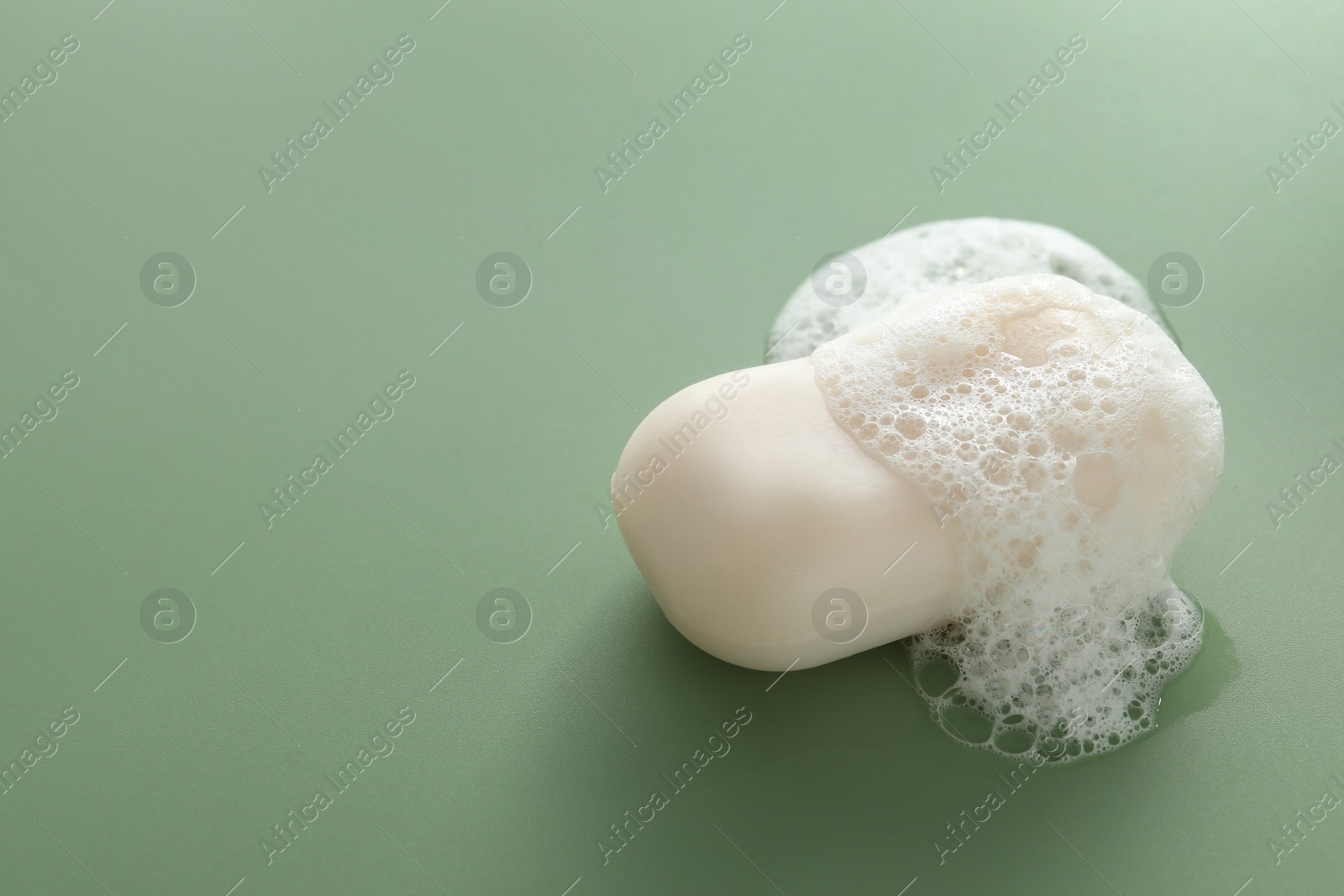 Photo of Soap bar with fluffy foam on green background, space for text