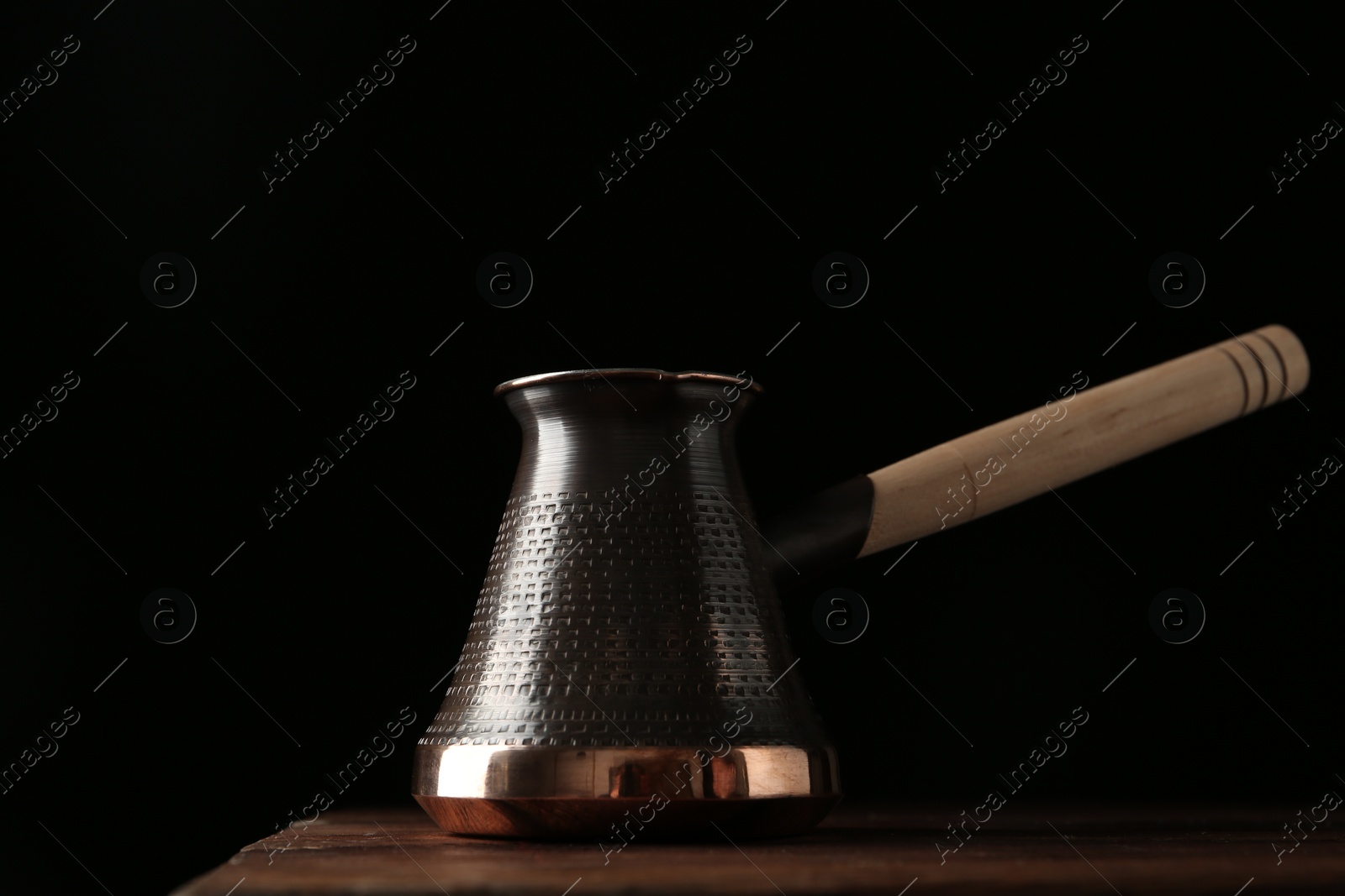 Photo of Beautiful copper turkish coffee pot on wooden table against dark background