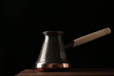 Beautiful copper turkish coffee pot on wooden table against dark background