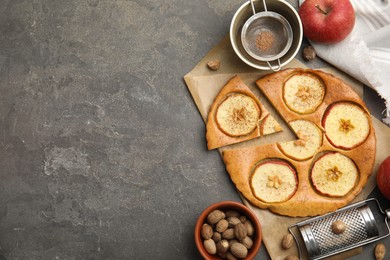 Photo of Nutmeg powder, seeds, tasty apple pie and fresh fruits on grey table, flat lay. Space for text