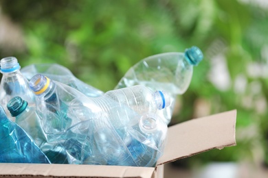 Photo of Cardboard box with used plastic bottles on blurred background. Recycling problem