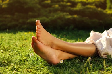 Photo of Woman sitting barefoot on green grass outdoors, closeup