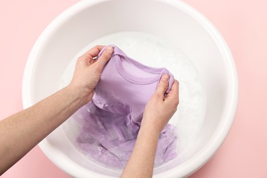 Photo of Woman washing baby clothes in basin on pink background, closeup