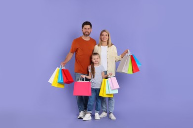 Family shopping. Happy parents and daughter with many colorful bags on violet background