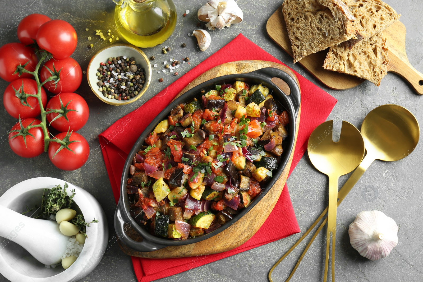 Photo of Dish with tasty ratatouille, ingredients and bread on grey textured table, flat lay
