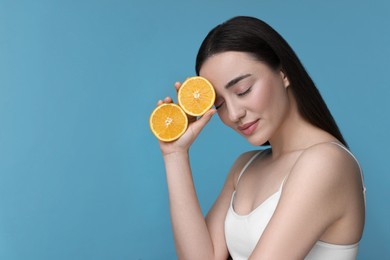 Photo of Beautiful young woman with pieces of orange on light blue background. Space for text