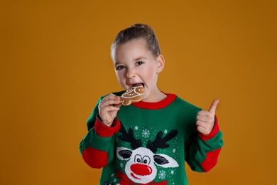 Cute little girl with Christmas gingerbread cookie on orange background