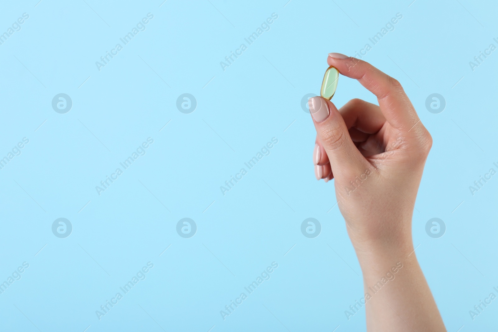 Photo of Woman holding vitamin capsule on light blue background, closeup with space for text. Health supplement