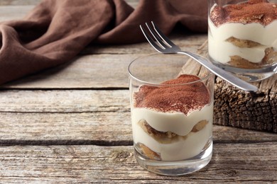 Delicious tiramisu in glasses and fork on wooden table, space for text