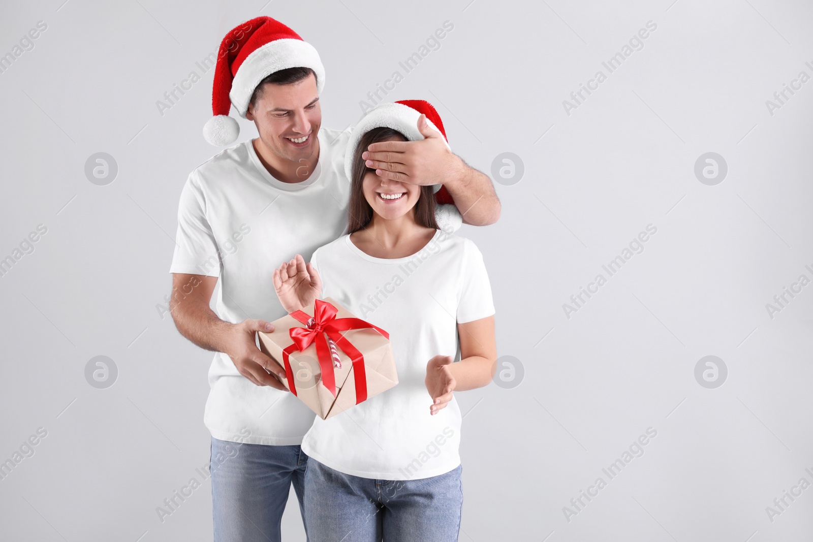 Photo of Man presenting Christmas gift to his girlfriend on light background