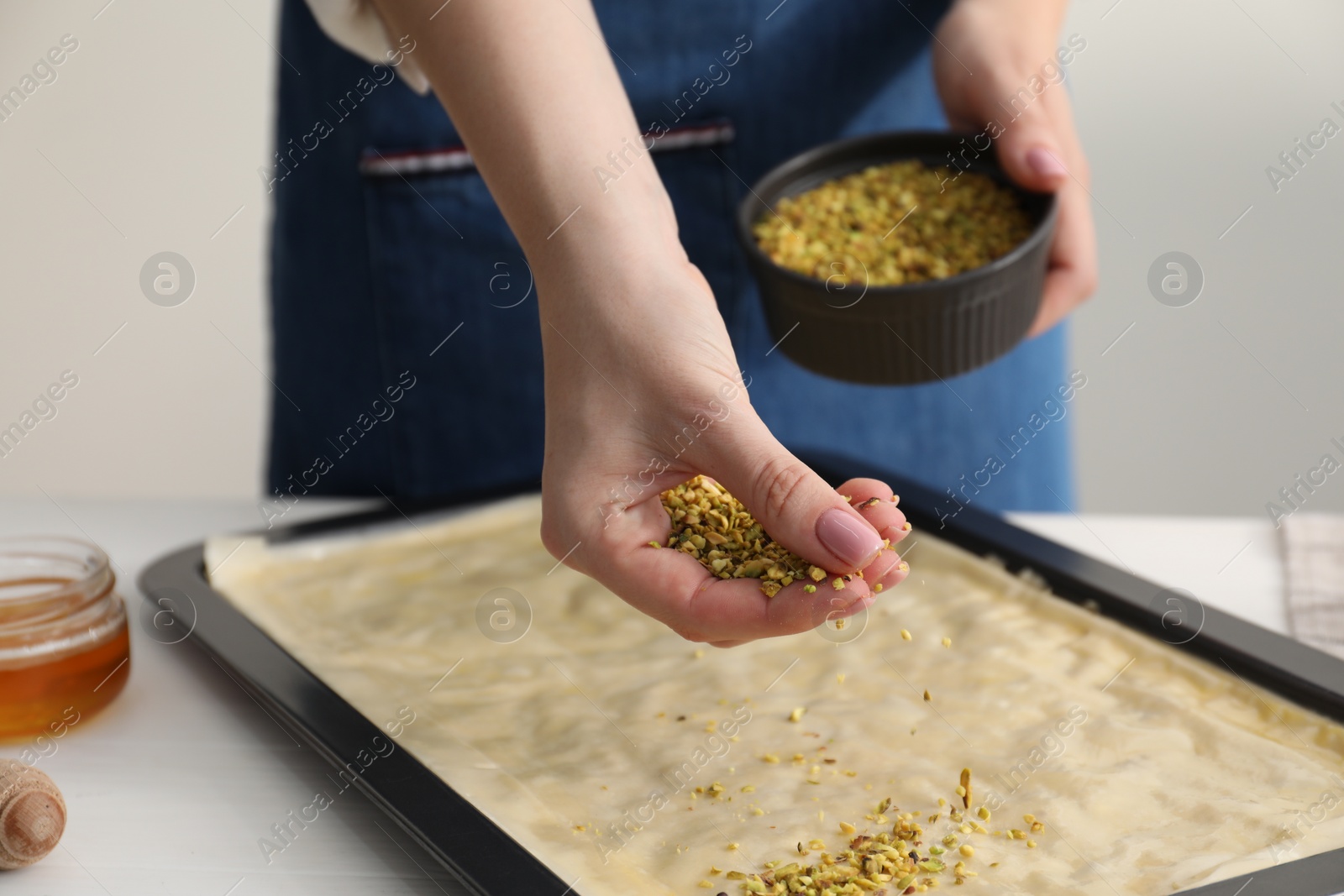 Photo of Making delicious baklava. Woman adding chopped nuts to dough at white table, closeup